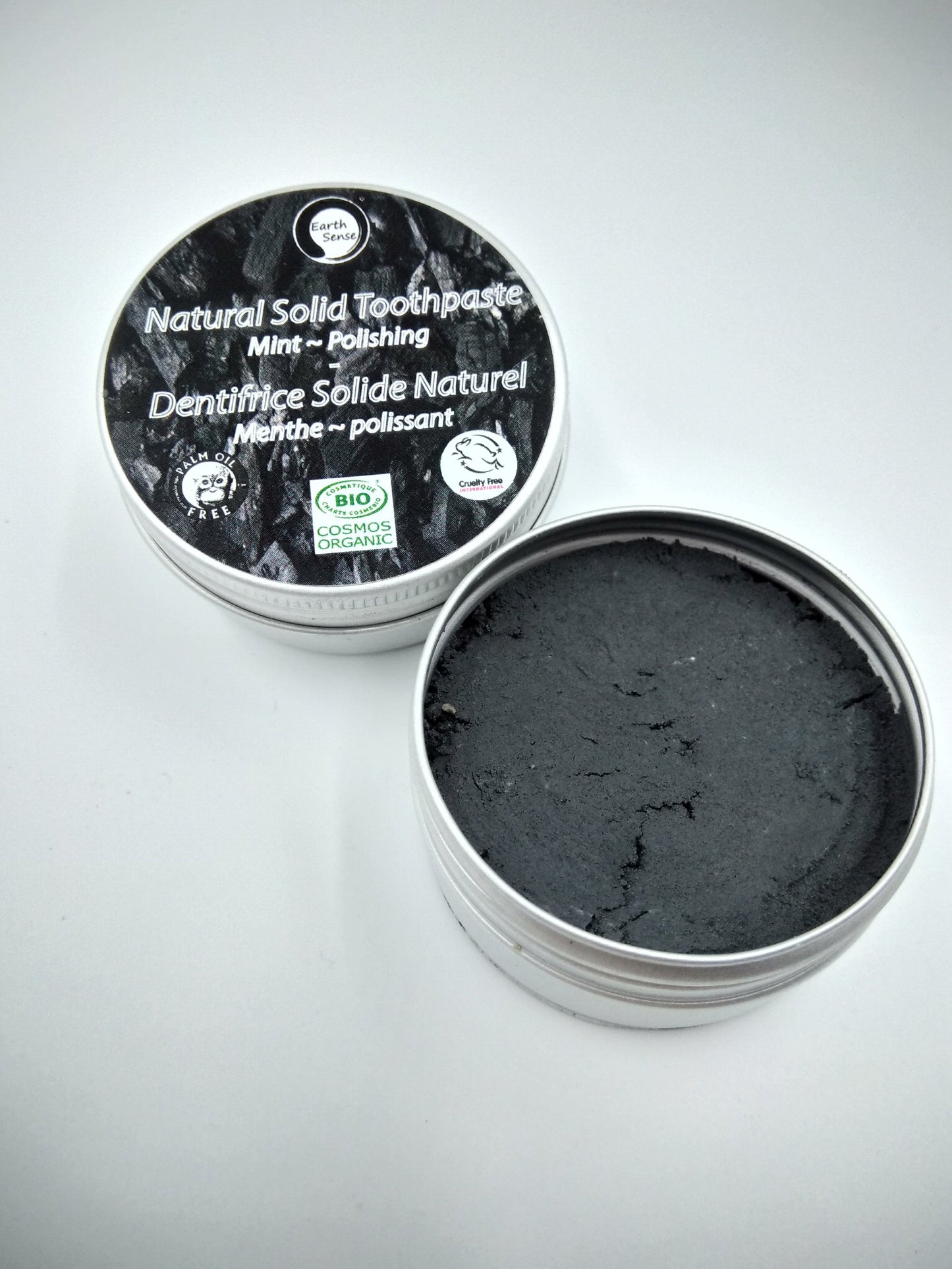 Open container of natural solid toothpaste with black paste inside on a gray background