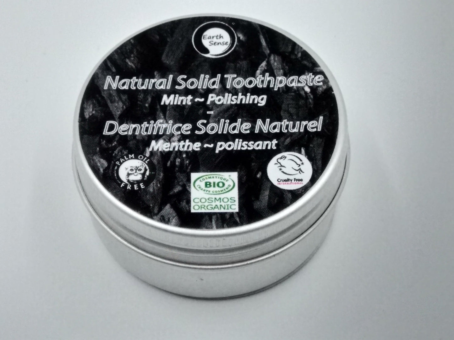Natural solid toothpaste container with black lid and silver body on a gray background