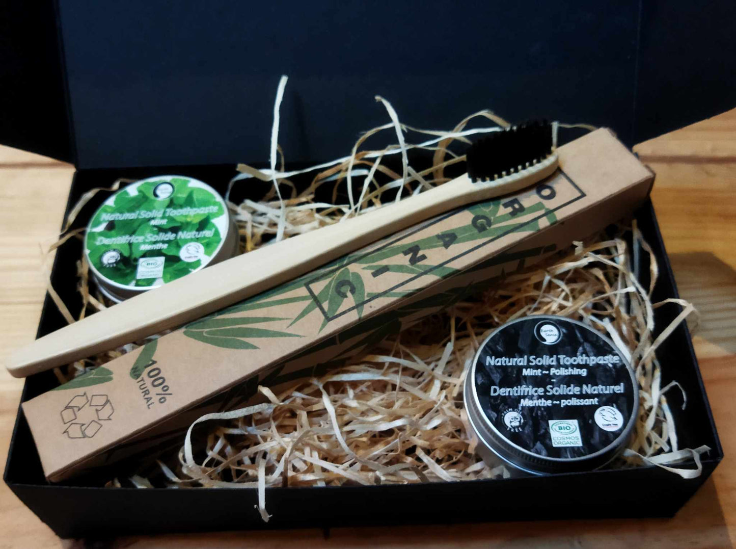 Set of natural solid toothpaste, wooden toothbrush, and packaging in a box on a wooden surface.