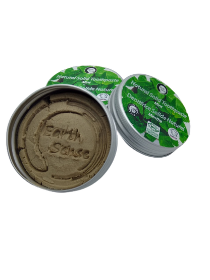 Open container of natural toothpaste with green lid on a white background