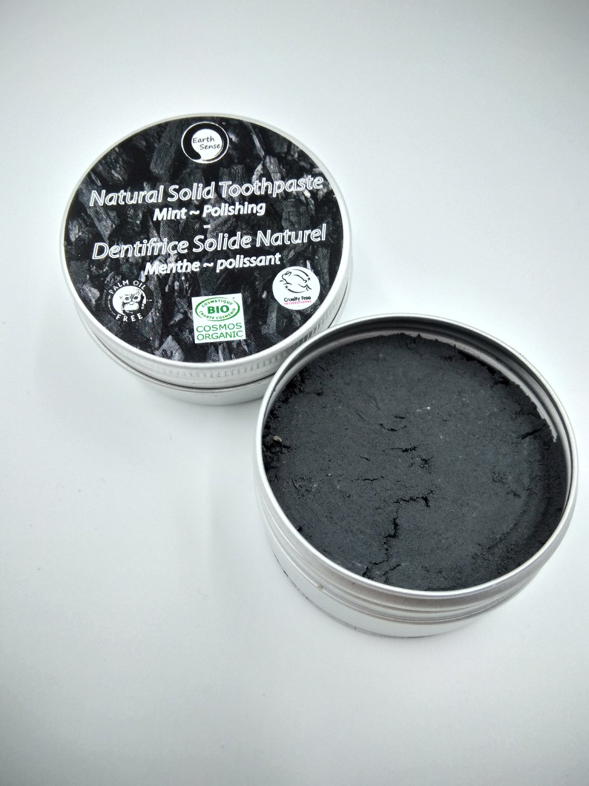 Open container of natural solid toothpaste with black paste inside on a gray background