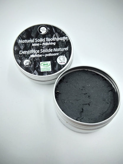 Open container of natural solid toothpaste with black paste inside on a gray background