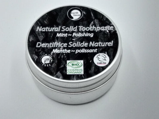 Natural solid toothpaste container with black lid and silver body on a gray background