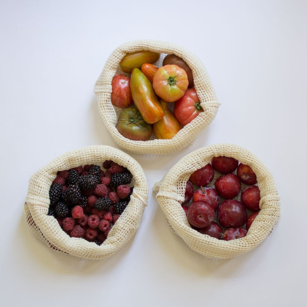 Three woven bags filled with fruits and berries on a white background