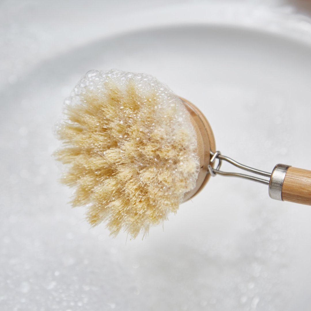 Dishwashing brush with a wooden handle and bristle head in soapy water